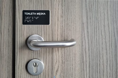 Tabliczka brajlowska biały napis na czarnym tle: toaleta męska